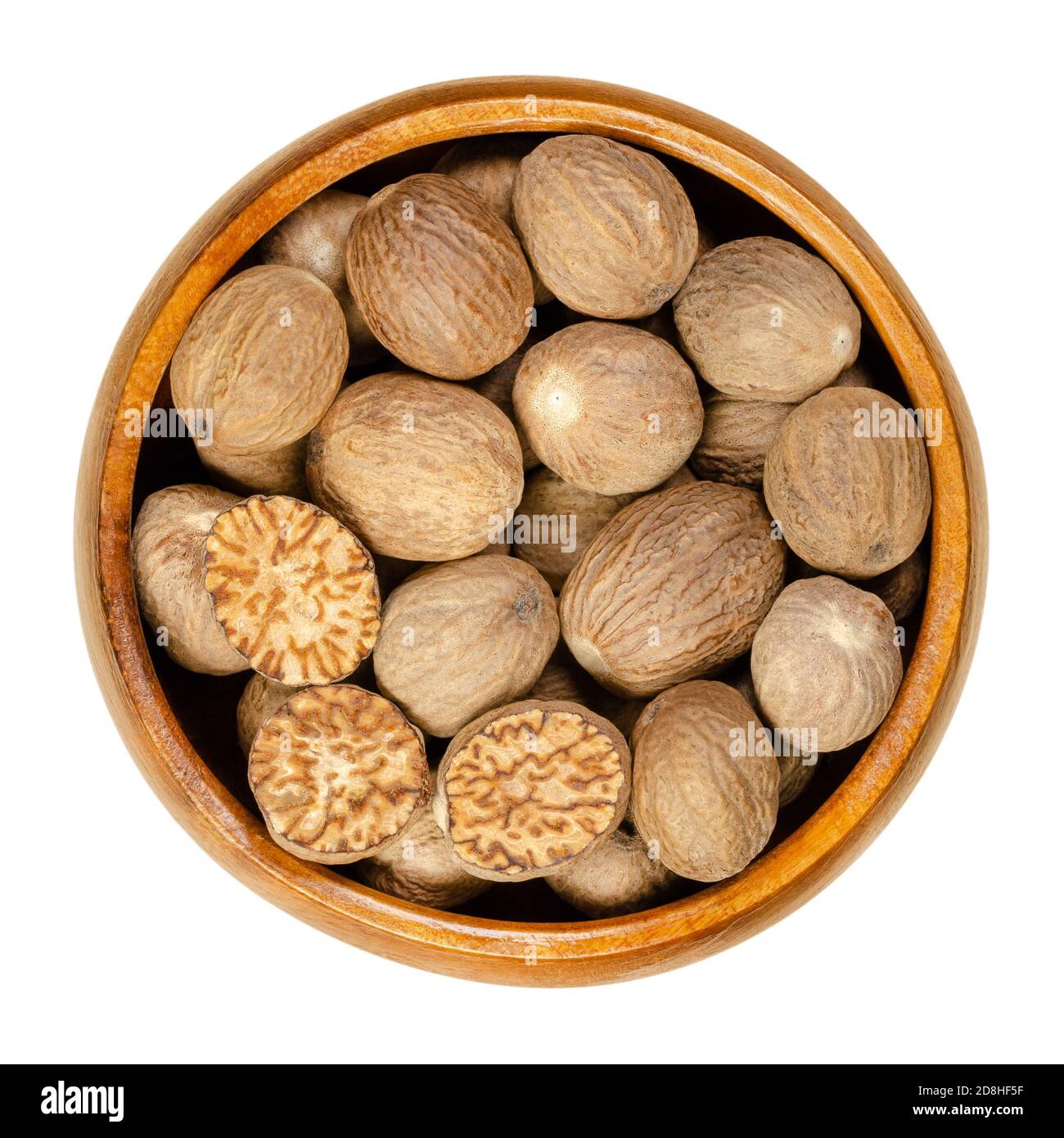 Whole and halved nutmegs in a wooden bowl. Fragrant or true nutmegs, dried seeds of Myristica fragrans, used as spice and in traditional medicine. Stock Photo