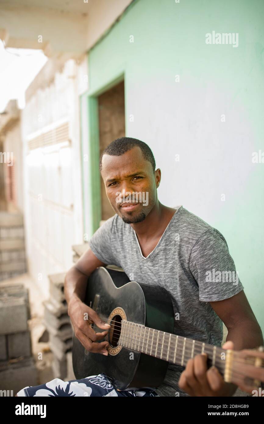 An adult male plays a guitar outside his home on Maio Island, Cabo Verde. Stock Photo