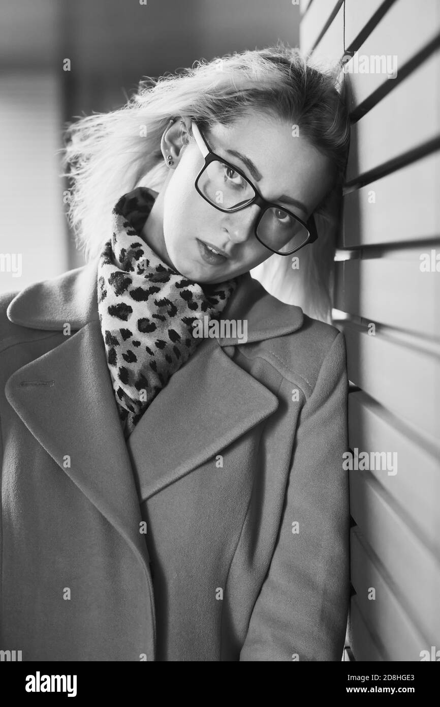 sad blonde woman with glasses near the wall looking at the camera, monochrome Stock Photo