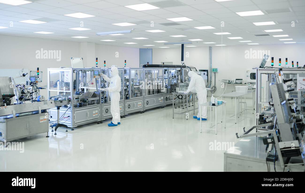 Shot Of Sterile High Precision Manufacturing Laboratory where Scientists in Protective Coverall's Use Computers and Microscopes, doing Pharmaceutics Stock Photo
