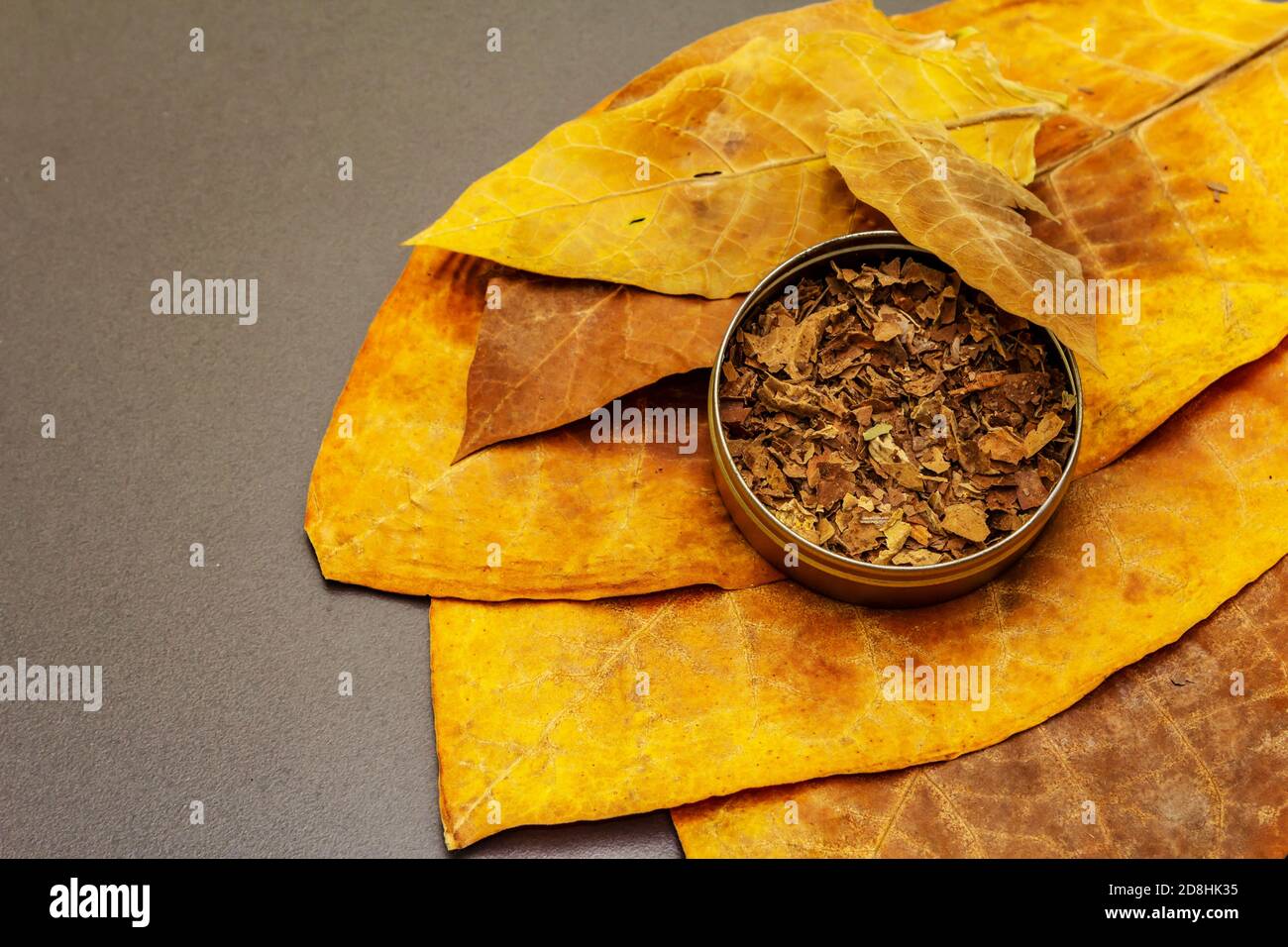 shredded tobacco leaves Shredded tobacco in a tin box. High quality cured big leaves to make  cigars. Black stone concrete background, copy space Stock Photo