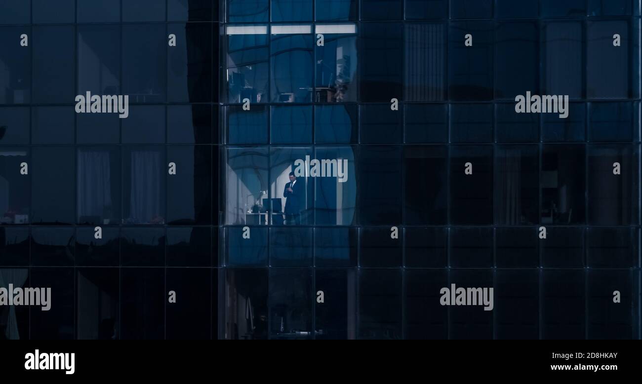 Aerial View Shot: From Outside into Office Building with Businessman Using Mobile Phone and Standing Next to the Office Window. Beautiful Shot of The Stock Photo