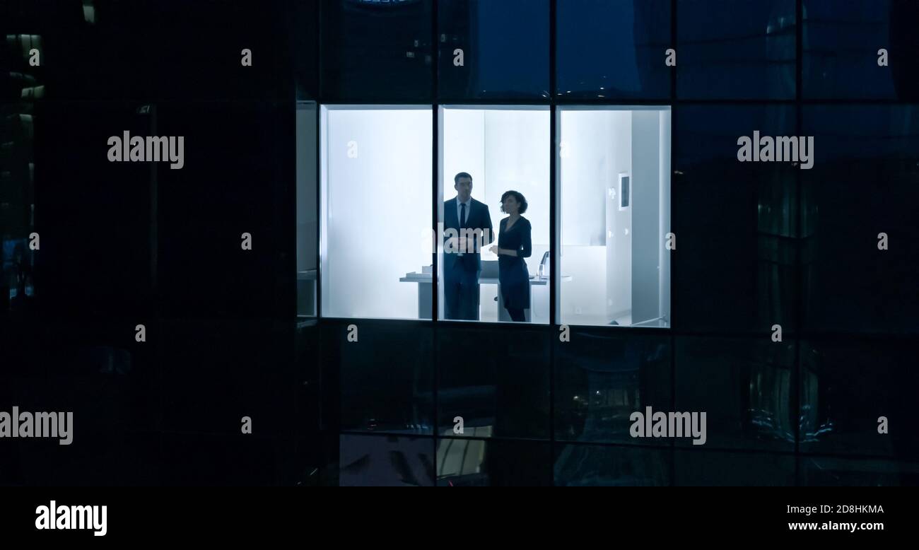 Aerial Shot From Outside of the Skyscraper: Businessman and Businesswoman Talking while Looking Out of the Office Window. Shot of the Business Stock Photo