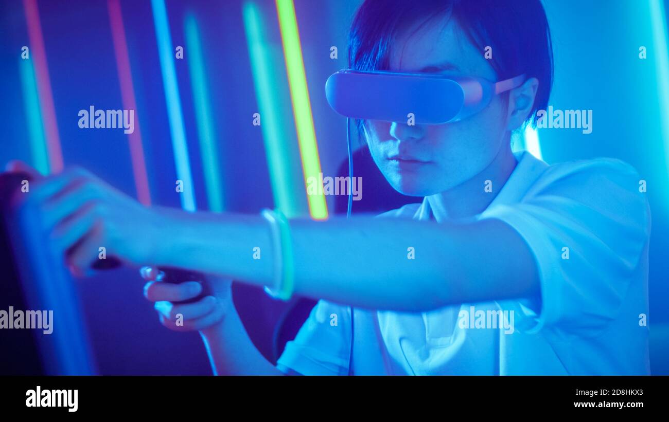 East Asian Pro Gamer Wearing Virtual Reality Headset Plays Online Video Game with Joysticks Controllers. Cool Retro Neon Colors in the Room. Stock Photo