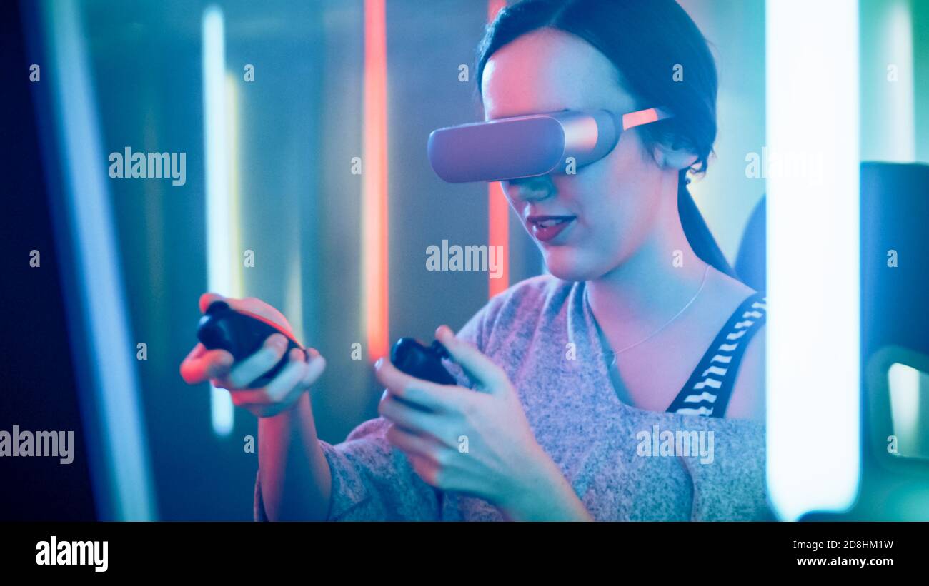 Pro Gamer Girl Wearing Virtual Reality Headset Plays Online Video Game with Joysticks Controllers. Cool Futuristic Neon Colors in the Room. Stock Photo