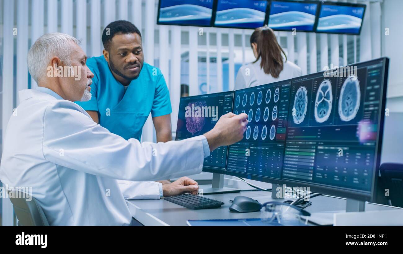 Medical Scientist and Surgeon Discussing CT MRI Brain Scan Images on a Personal Computer in Laboratory. Neurologists Neuroscientists in Neurological Stock Photo