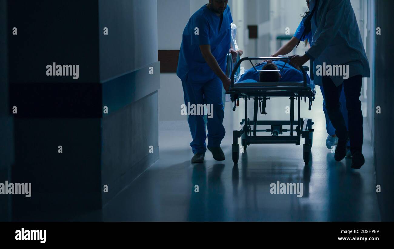 Emergency Department: Doctors, Nurses and Paramedics Push Gurney Stretcher with Seriously Injured Patient towards the Operating Room. Stock Photo