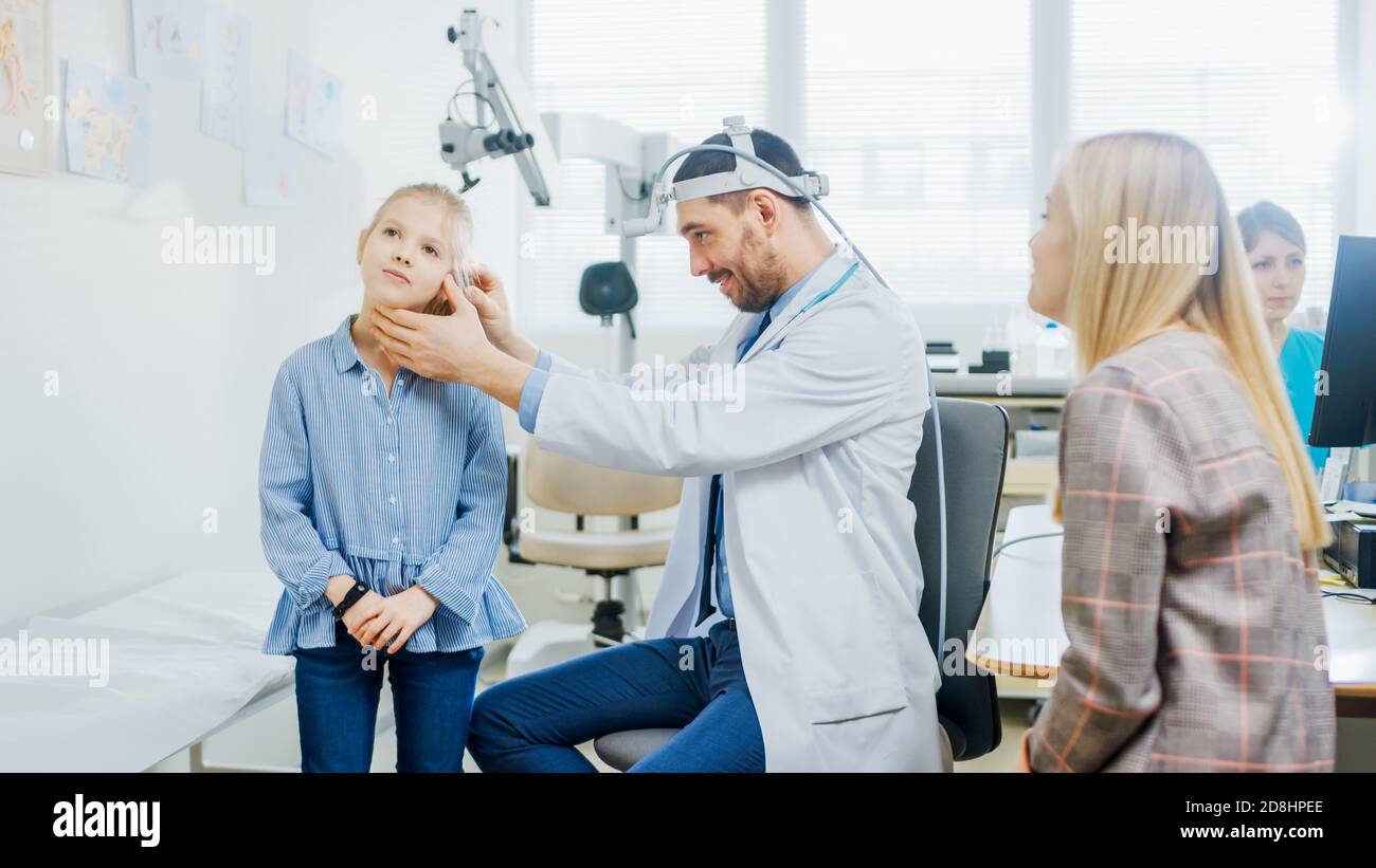 Mother with a Little Daughter Visit Doctor. Friendly ENT Pediatrician Checks Ears of a Little Smiling Girl. Child Health Examination Using Special Stock Photo