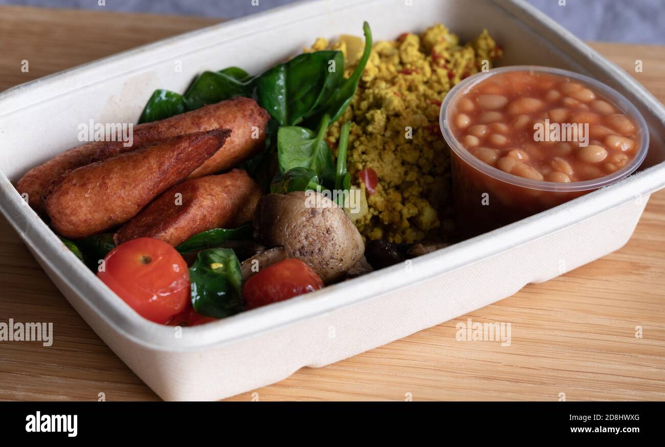 Cooked vegan breakfast, with vegan sausages, baked beans, fried mushrooms, scrambled tofu, tomatoes and spinach. Served in recyclable cardboard box Stock Photo