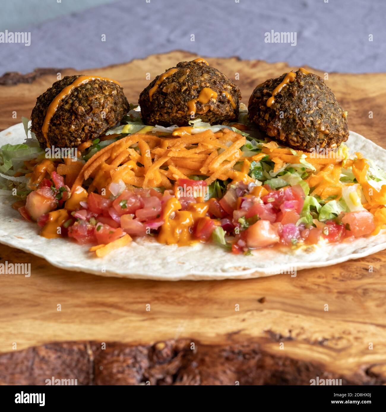 Fried falafal balls with colourful salad in a wrap, with sauce over. Stock Photo