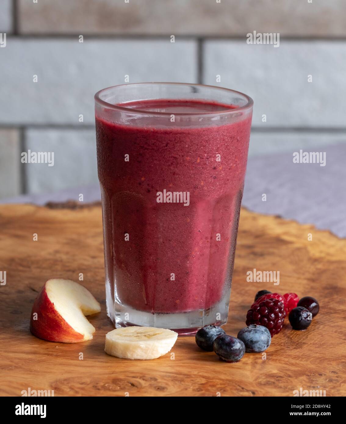 Glass of berry, banana and apple smoothie, served on a wooden platter. Stock Photo