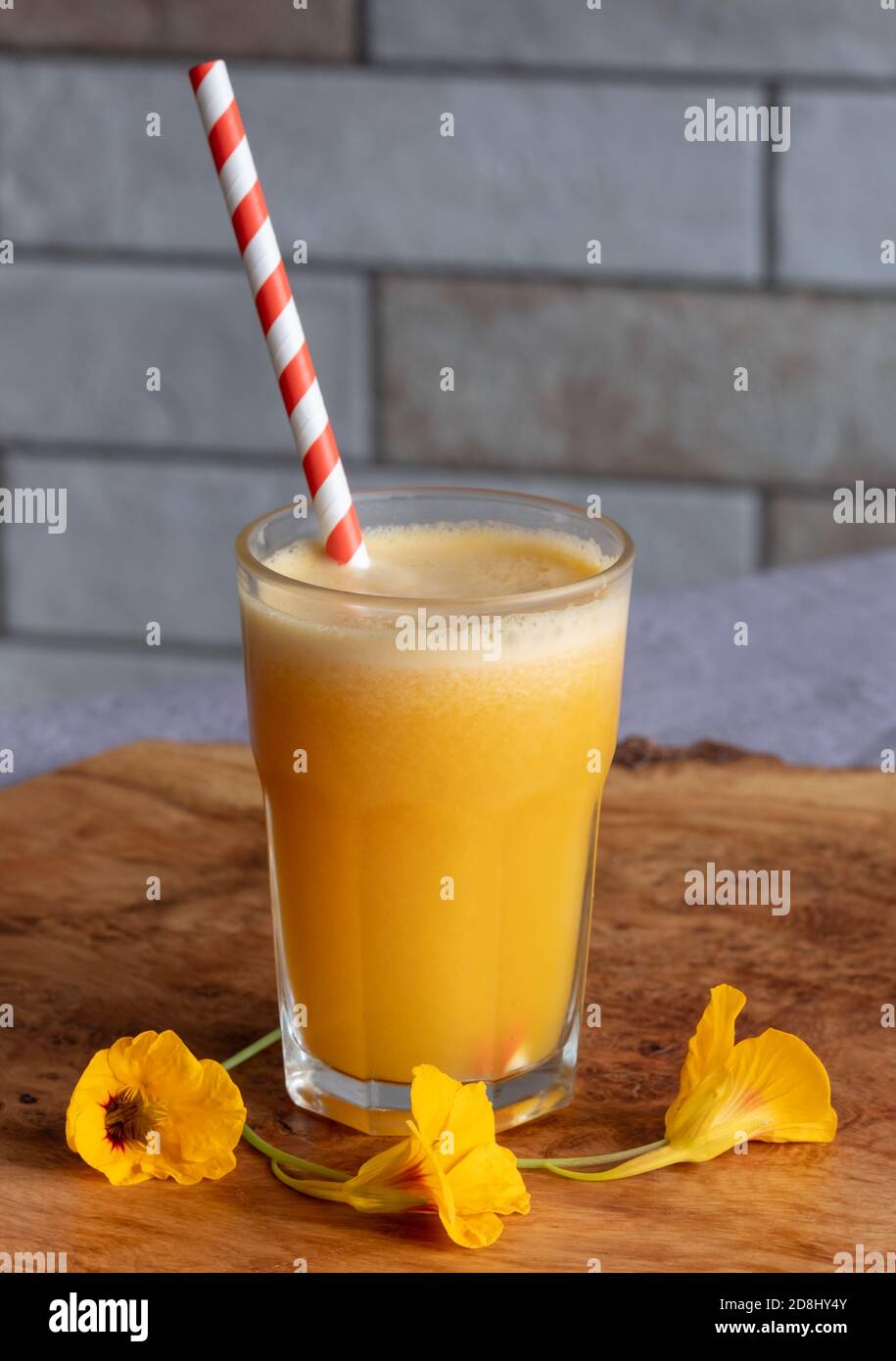 Fresh orange juice with paper straw, served on an olive wood platter with orange nasturtium flowers. Stock Photo