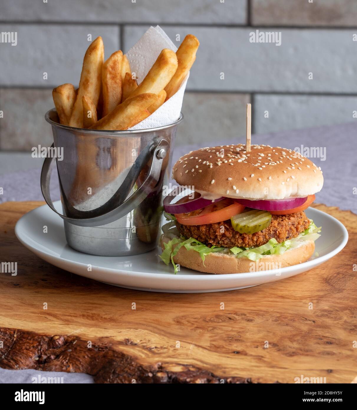 Vegan veggie soya burger in bun with salad and relish, and chips on the side. Vertical view. Stock Photo