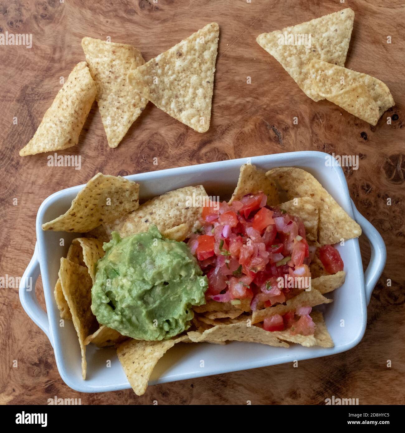 Nachos with avocado guacamole and salsa, served in a white bowl on a wooden platter. Stock Photo