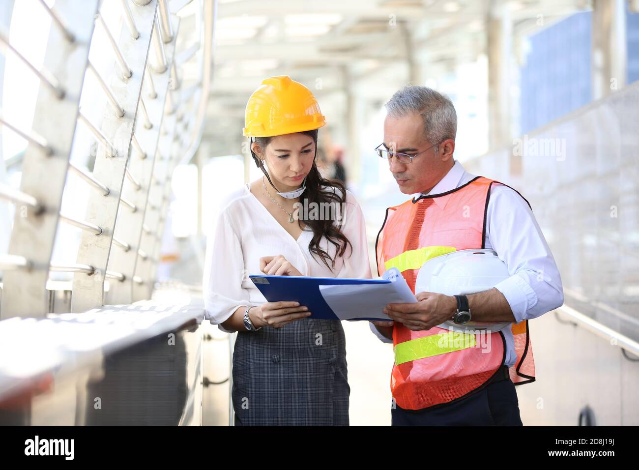 Female industrial engineer wearing a white helmet while standing in a construction site with businessman talking on working plan, Engineer and archite Stock Photo