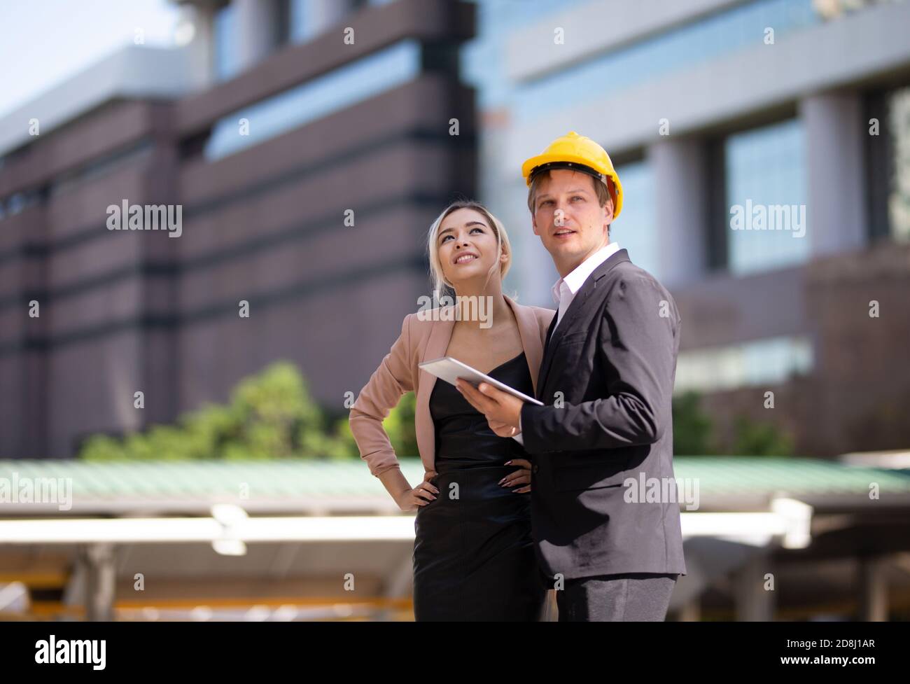 Female industrial engineer wearing a white helmet while standing in a construction site with businessman talking on working plan, Engineer and archite Stock Photo