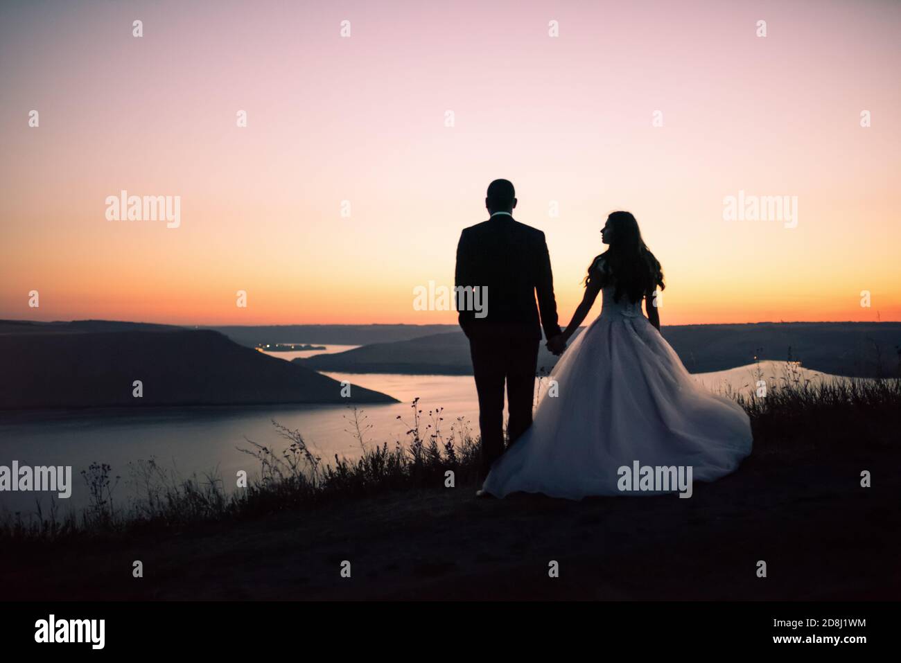 Silhouettes of bride and groom at night against lake and islands Stock Photo