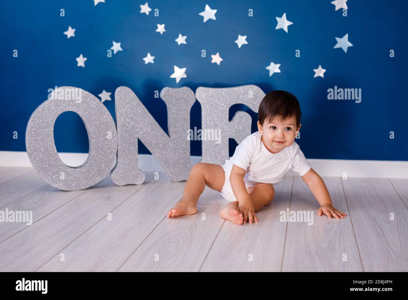 One year old baby boy celebrates birthday near silver letters ONE