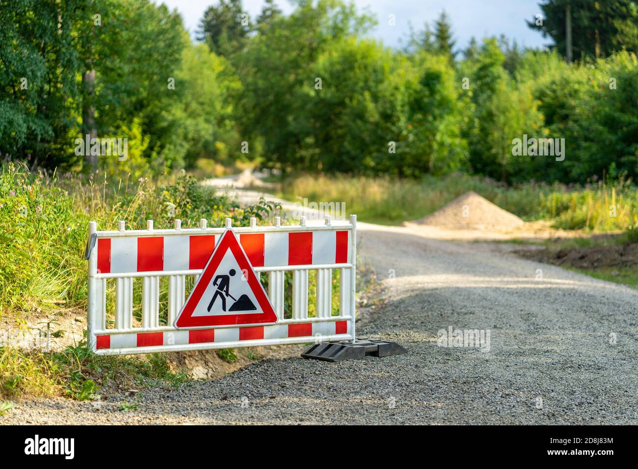 Men at work sign next to a pile of sand in a green area Stock Photo