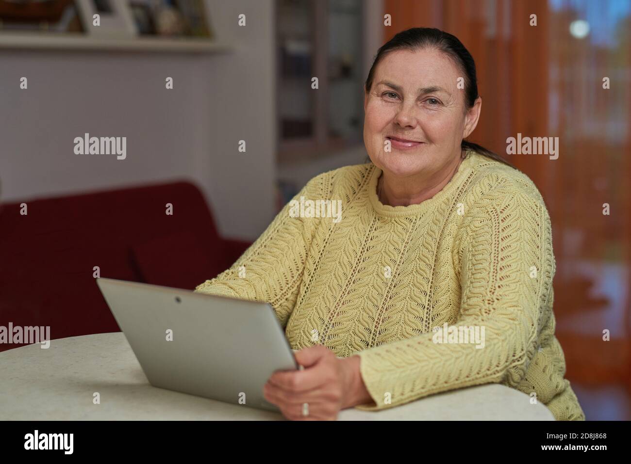 Senior woman in yellow sweater looking in the camera with tablet Stock Photo