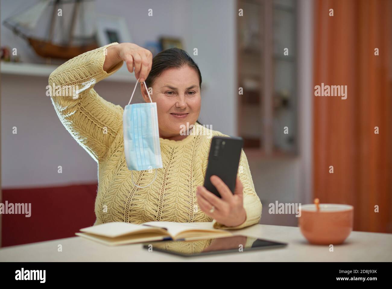 Senior woman looking at smartphone showing blue mask Stock Photo