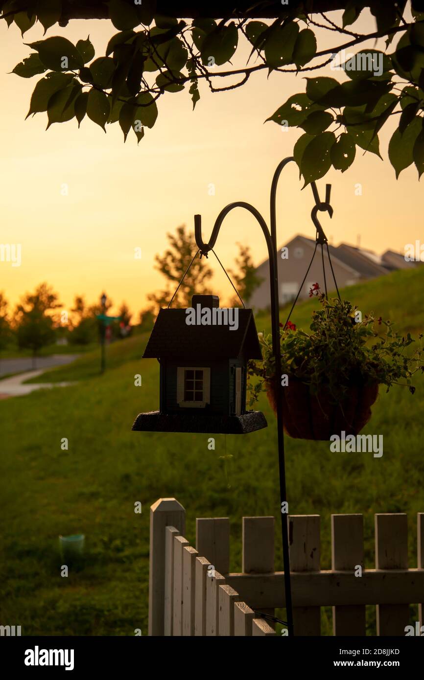 An abstract concept image taken at sunset showing a stand alone metal hanger rack with a bird house and a flower pot attached to it. The rack is place Stock Photo