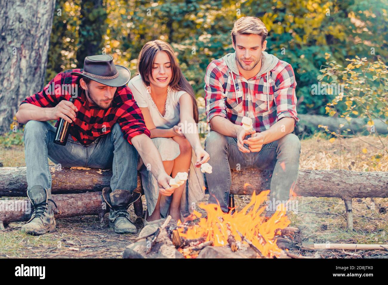 Happy young friends having picnic. Group of friends enjoying picnic in the forest. Happy friends on a camping trip relaxing by campfire. Company Stock Photo