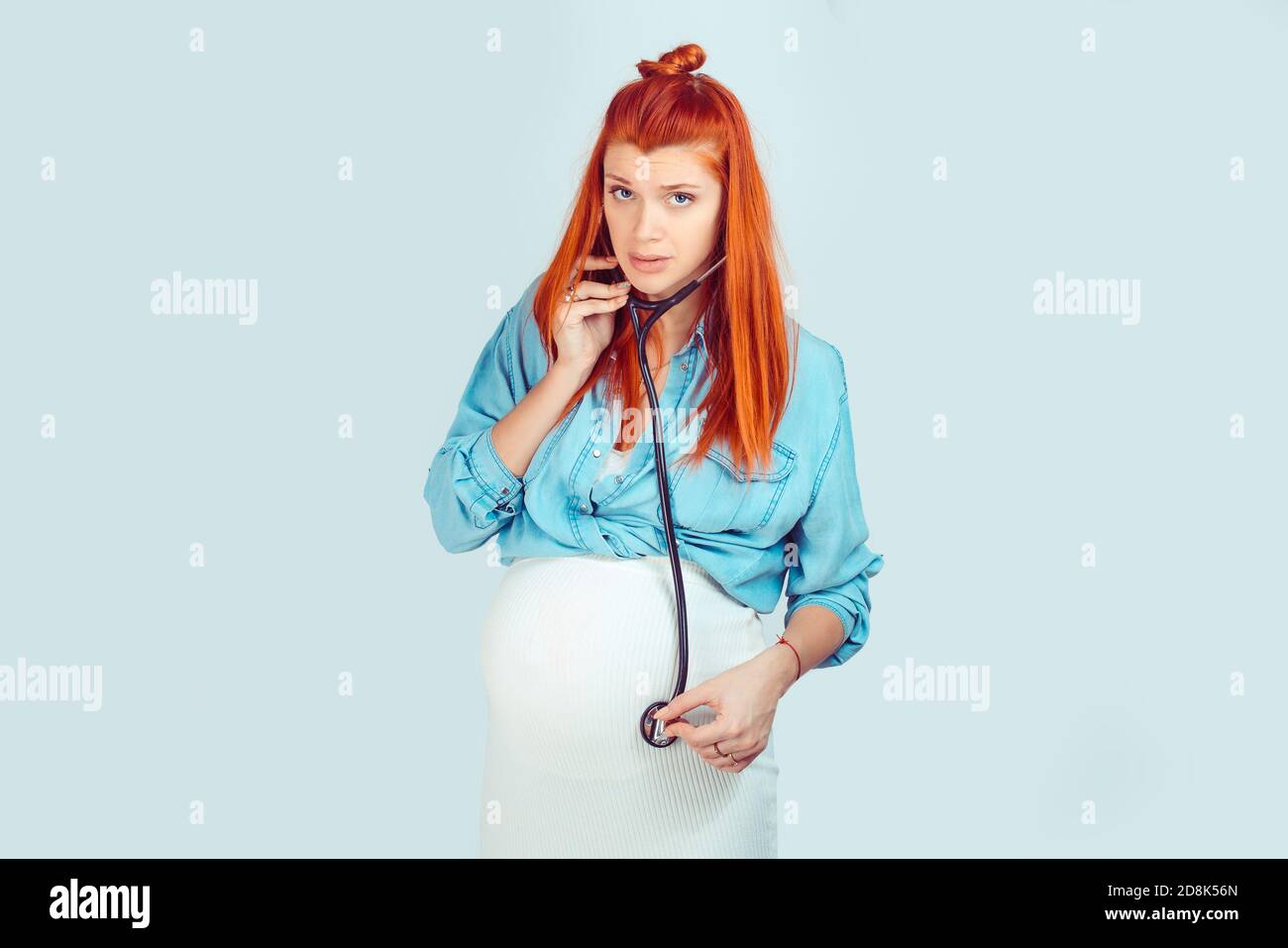 Young ginger pregnant woman using stethoscope and listening to baby