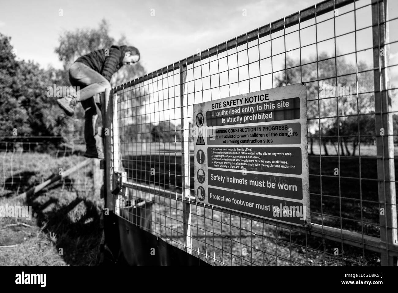 Adult male climbing fence into a contaminated heathland used for military training. Stock Photo