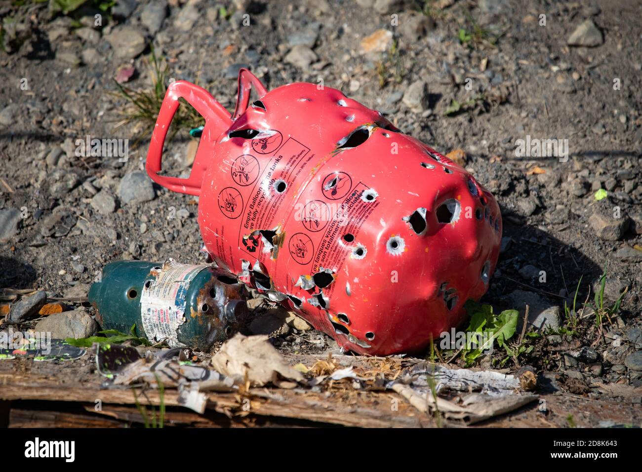 Red metal gas tank with bullet holes from backyard target practicing