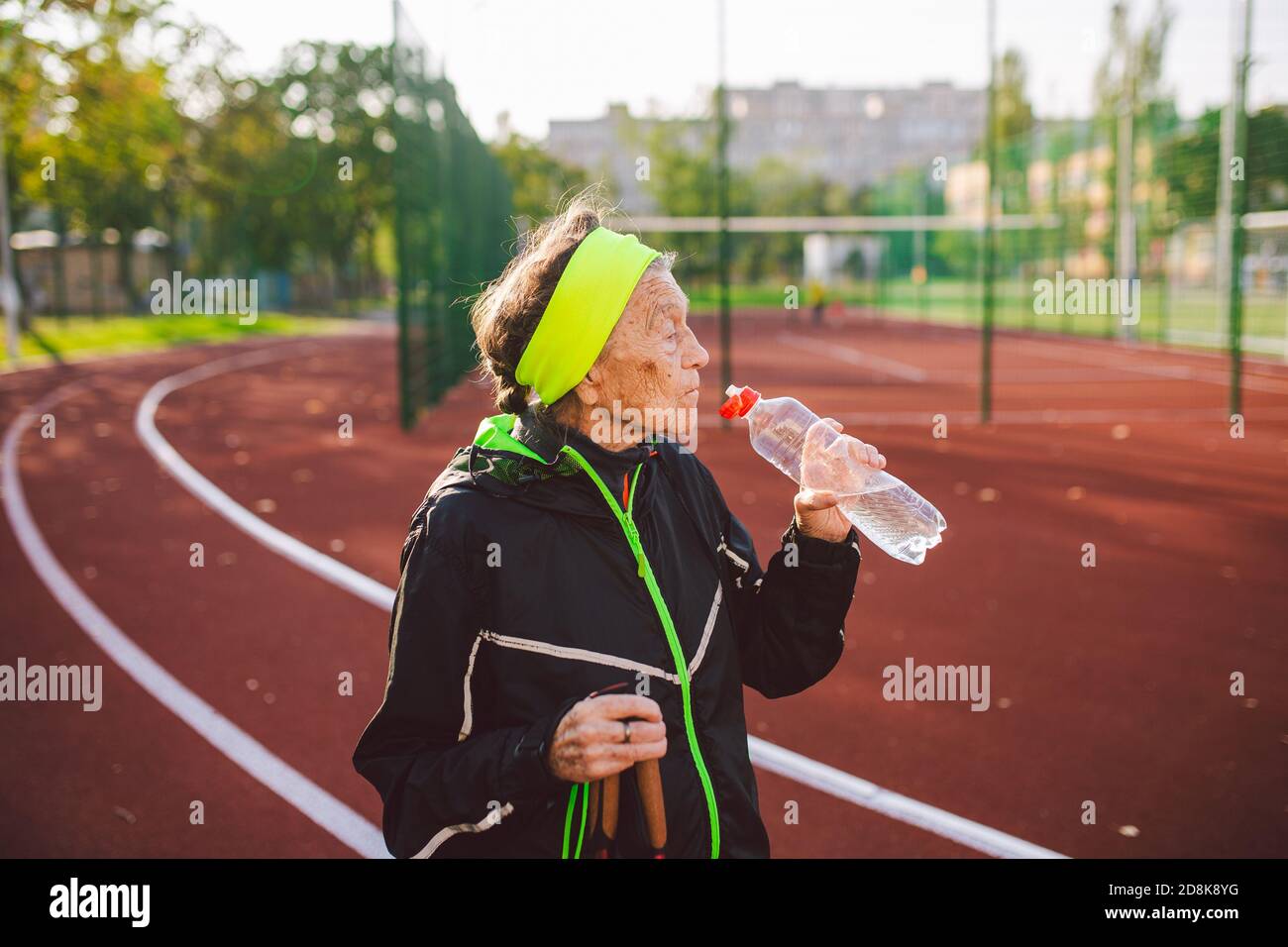 Age maturity, active lifestyle and wellness. Joyful retired woman with walking poles and bottle of water, refreshing during physical activity. Elderly Stock Photo