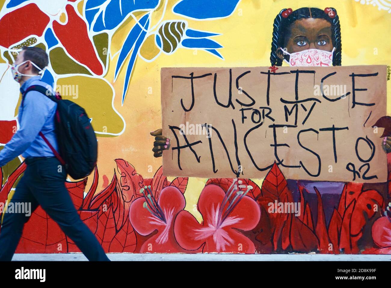 Black Lives Matter mural in downtown Oakland of an African American girl holding a sign that says 'Justice for my Ancestor' as pedestrian walks by. Stock Photo