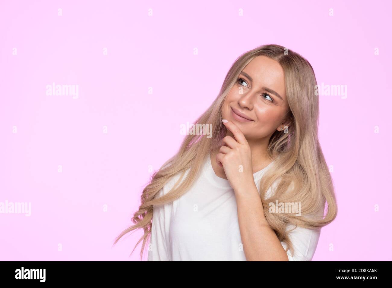 Closeup studio portrait of pensive young blonde female touching her chin, thinking, smiling, pondering and looking up, place for advertising or copy s Stock Photo