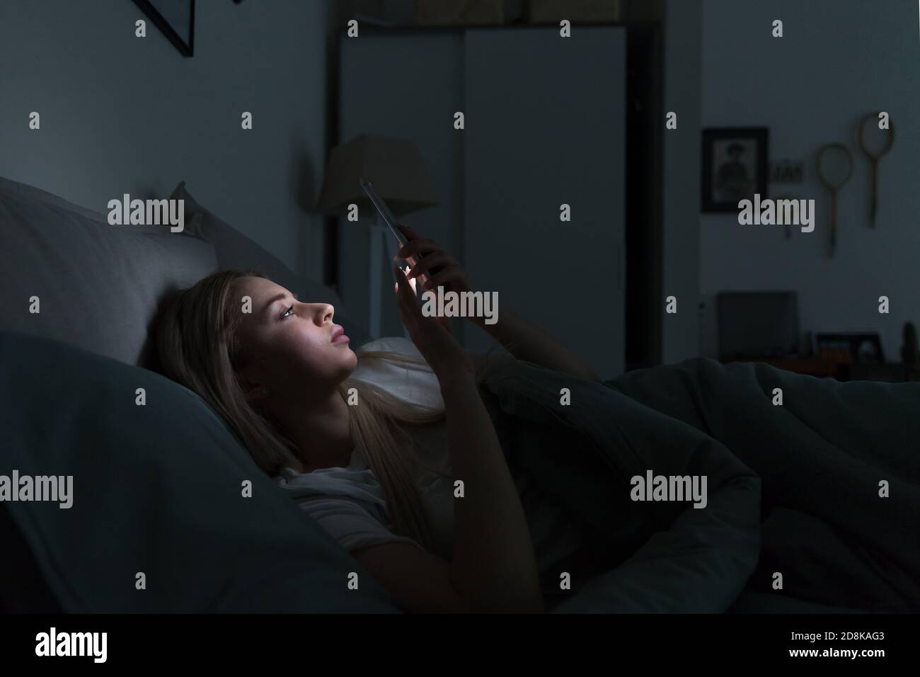 Sleepy exhausted woman lying in bed using smartphone at late night, can