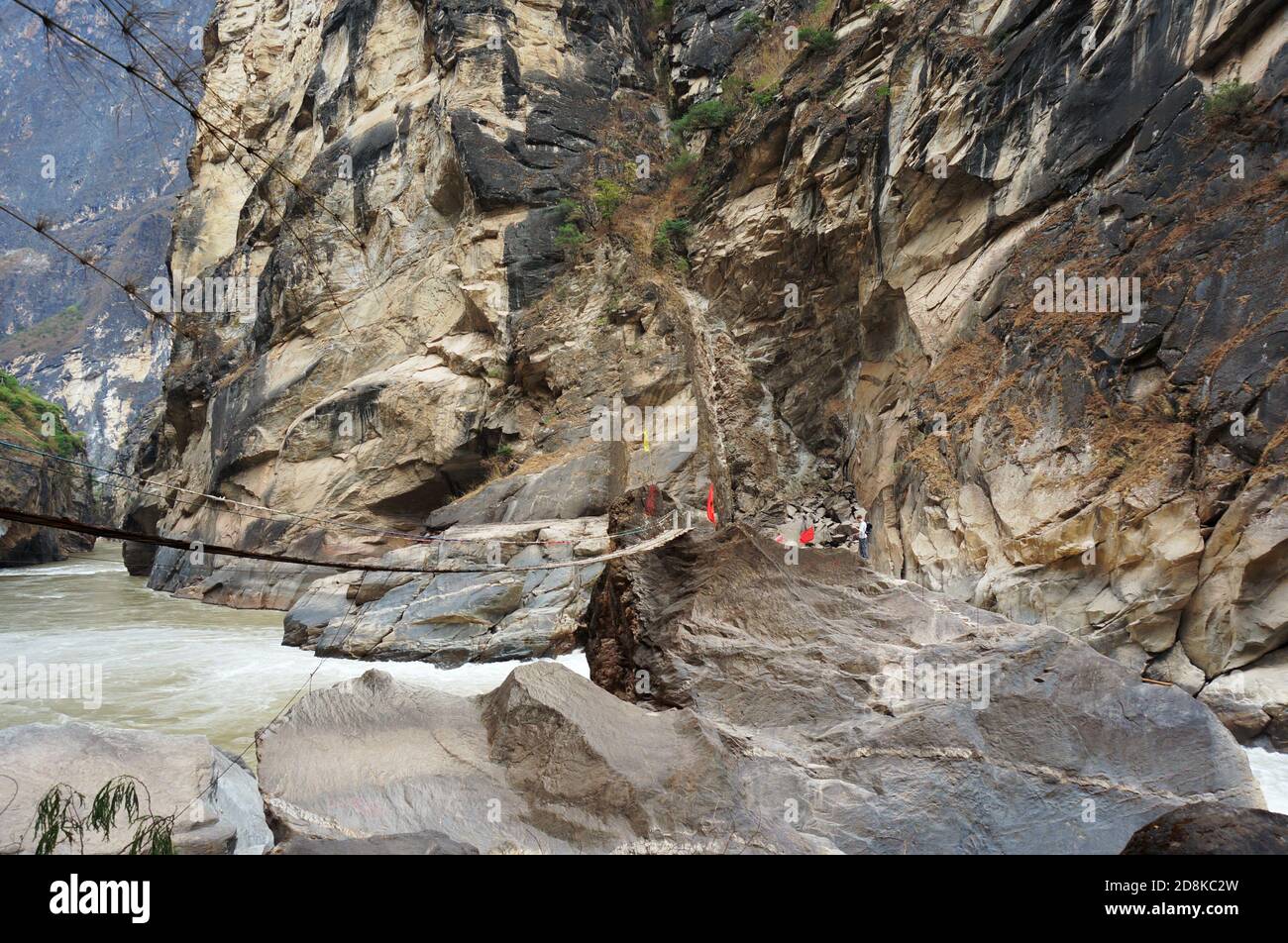 Rope bridge over the mountain river. Giant high rock formation. Brown cliffs wall Stock Photo
