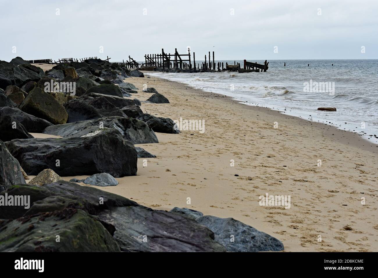 Large boulders and old wooden sea defences to prevent costal erosion of the cliffs along Happisburgh Beach, Norfolk, UK. Stock Photo