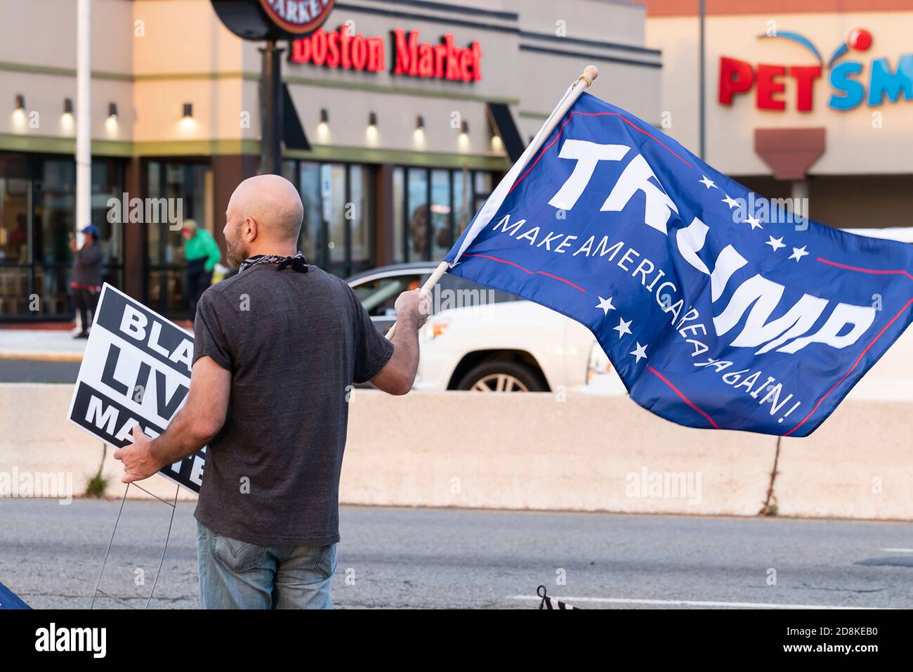 Donald Trump supporter holding 'Black Lives Matter' sign and 'TRUMP - Make America Great Again' flag at local sidewalk rally. Stock Photo