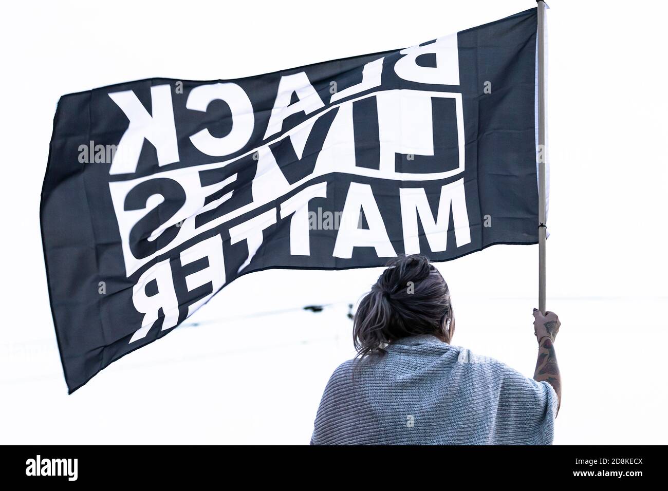 Person holds large 'BLACK LIVES MATTER' flag overhead at local sidewalk rally. Stock Photo