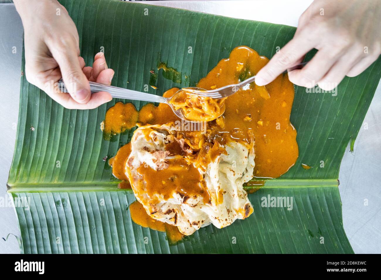 Person eating roti canai or paratha with curry on banana leaf, favourite Malaysian food Stock Photo