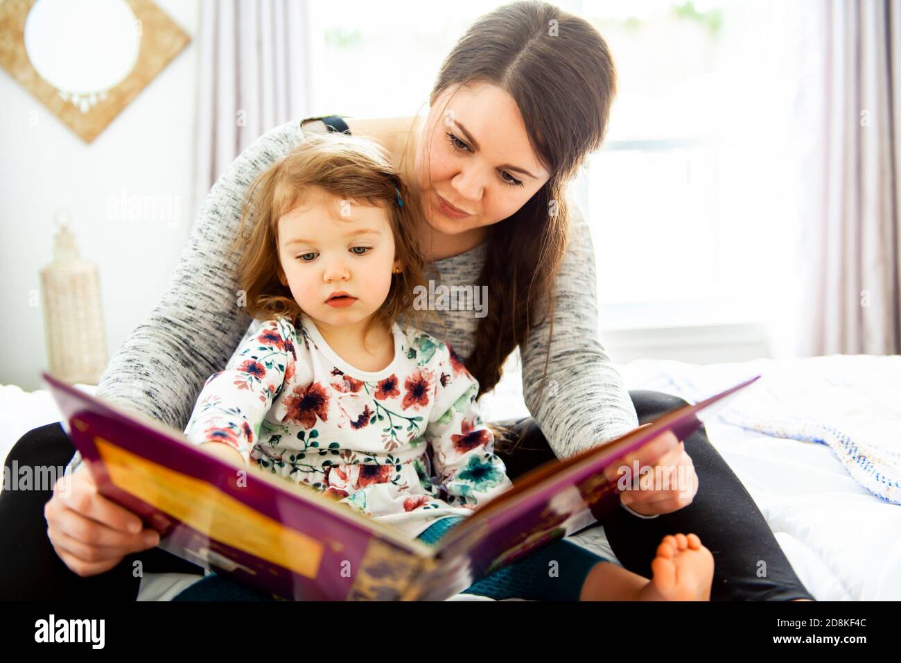 A mother and child daughter reading book in bed before going to sleep