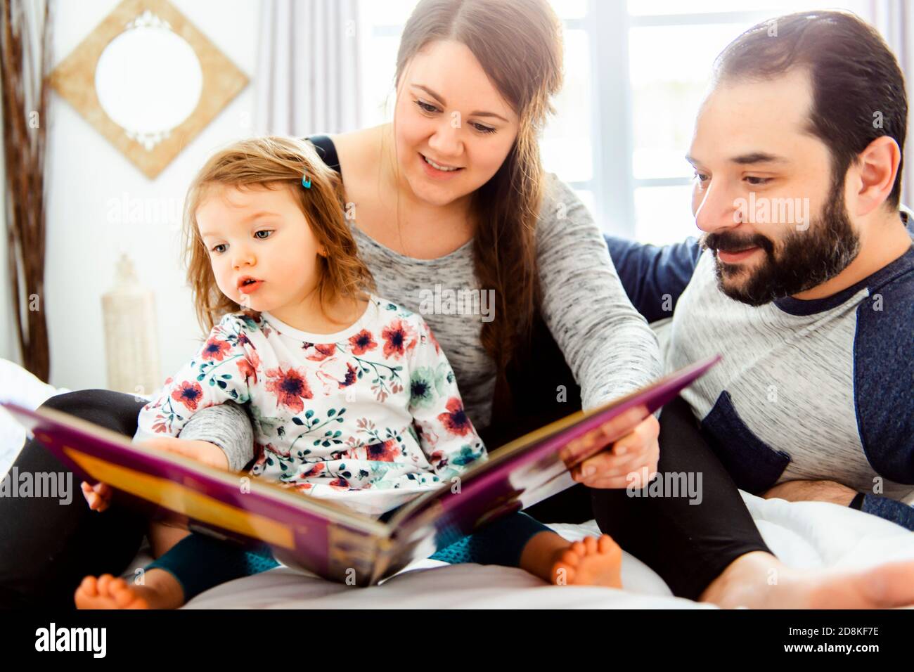A mother father and child daughter reading book in bed before going to