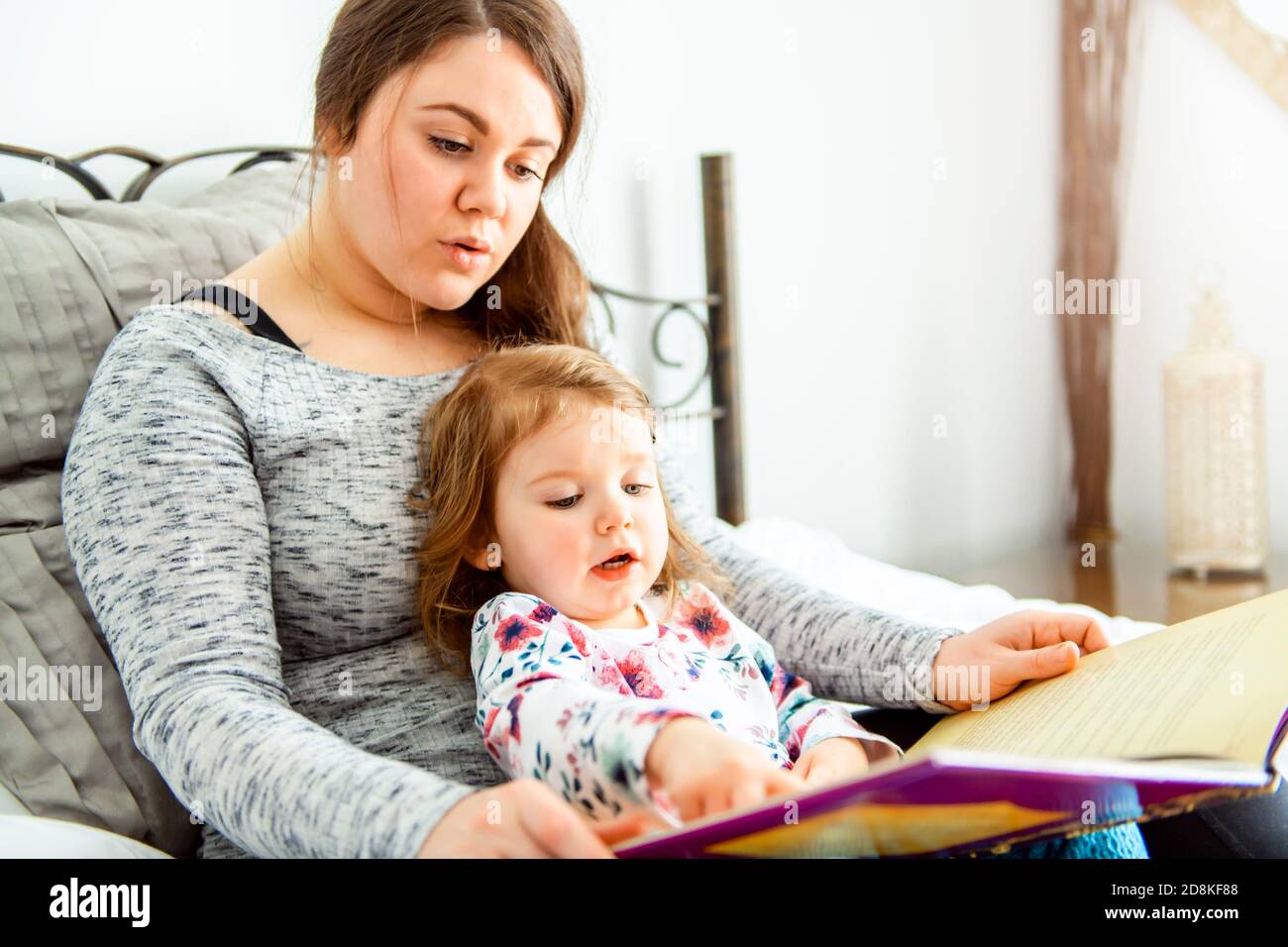 A mother and child daughter reading book in bed before going to sleep