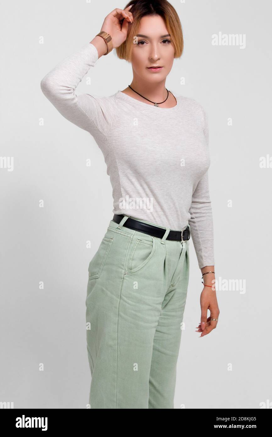 Portrait of a young woman with short hair. In a white sweater and green trousers. On white background. he holds his head in his hands Stock Photo