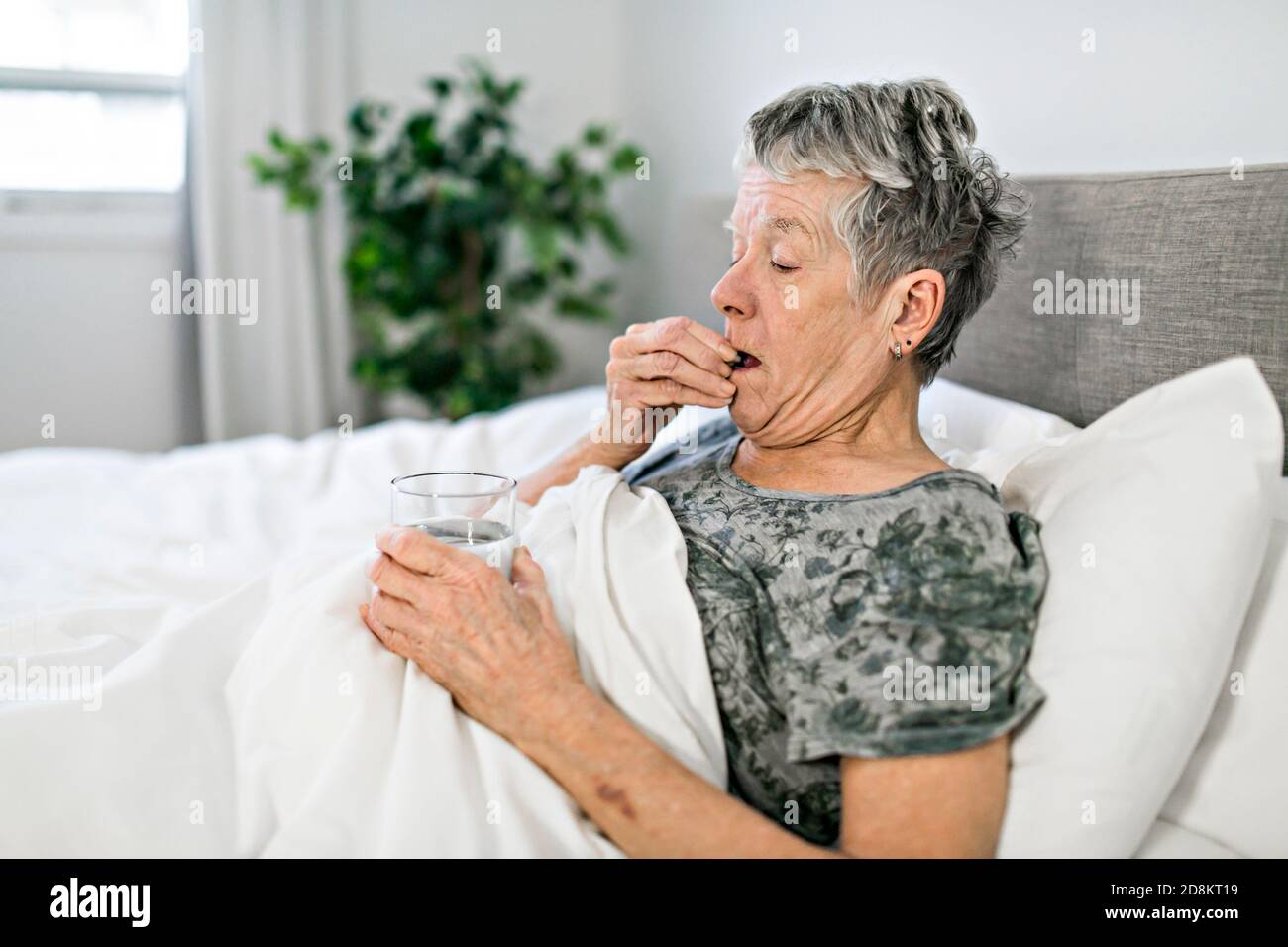 Unhealthy mature woman lying in bed, taking medicine from cold or