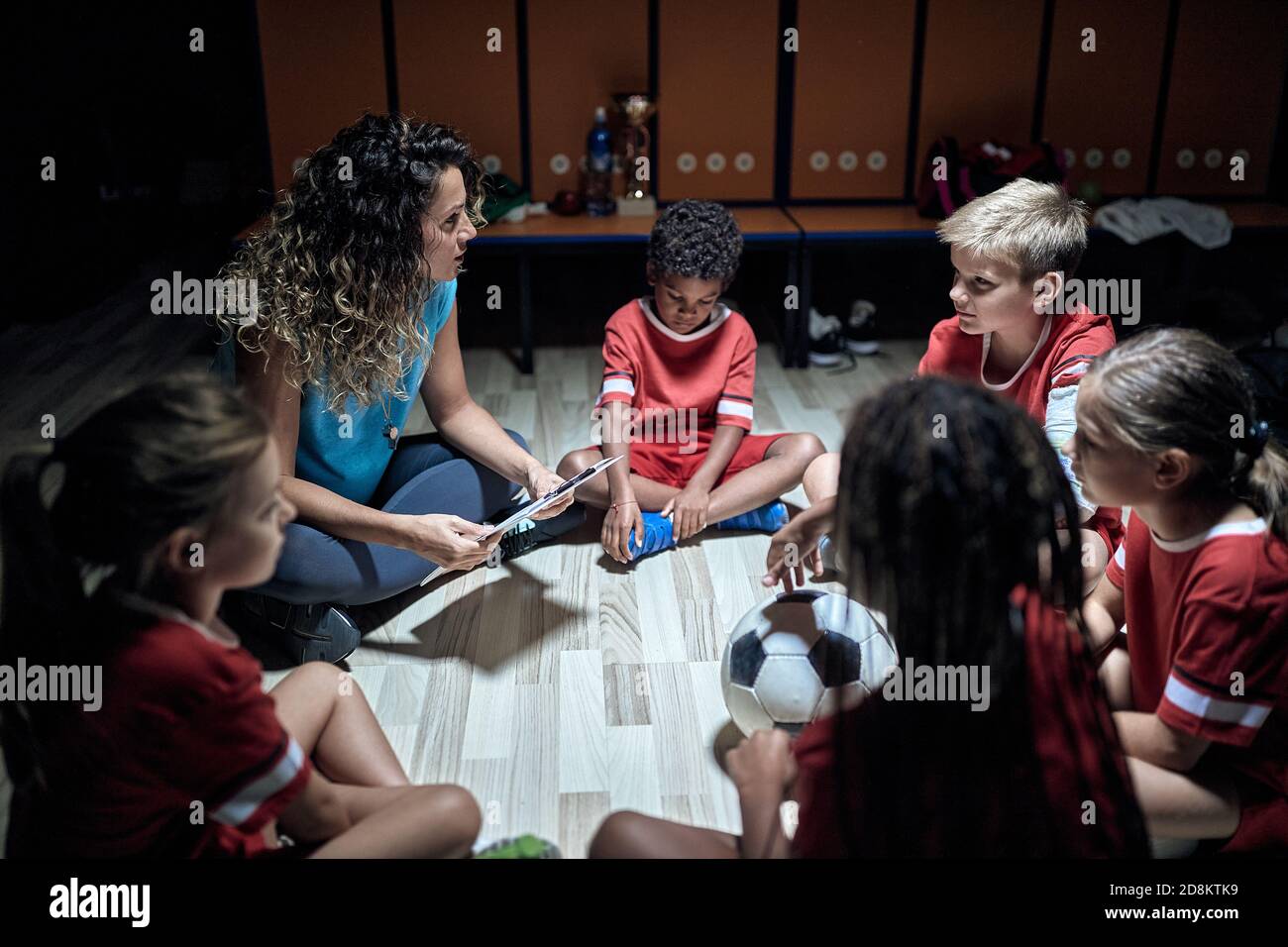 A female coach and her little players at the locker room discussing strategy for the match. Children team sport Stock Photo