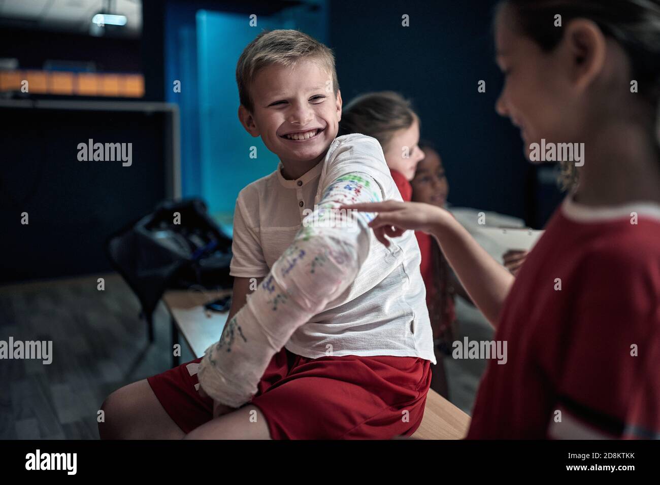 Little teammates at the locker room watching autographs on broken arm in gypsum. Children team sport Stock Photo