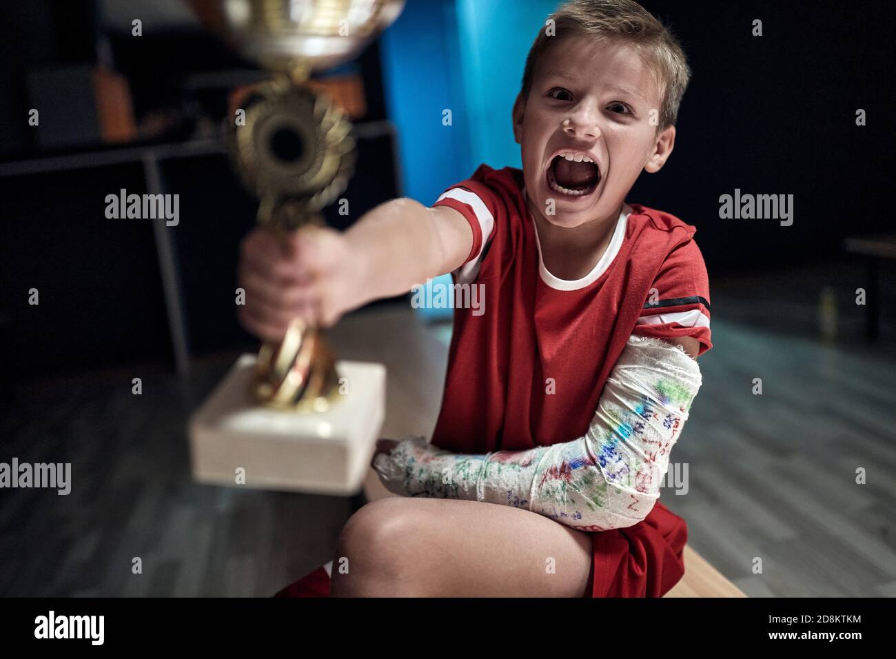 Excited little player at the locker room holding the trophy won in the match. Children team sport Stock Photo