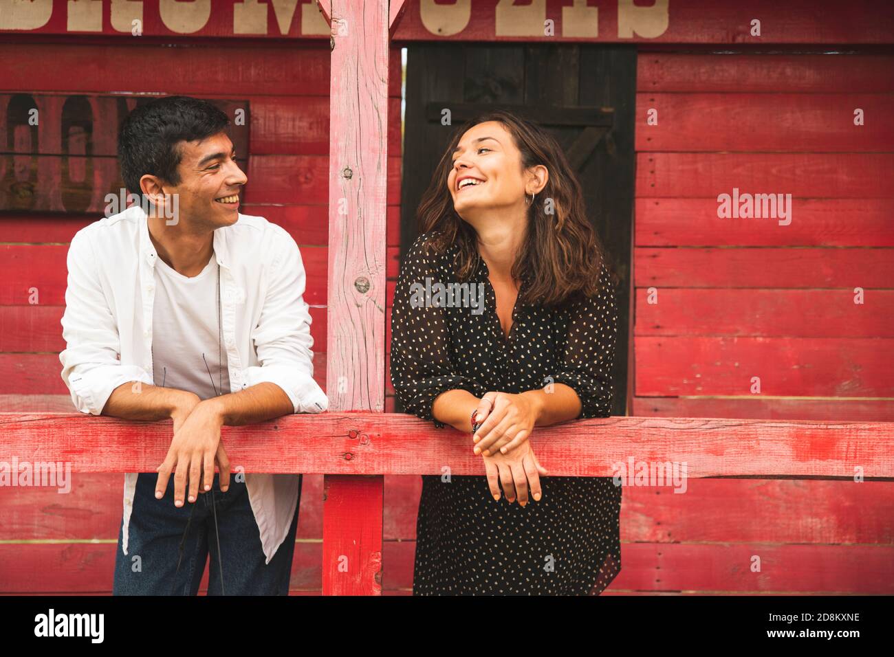 Pretty Couple Flirting and Smiling Each Other Outside of a Red Wooden Saloon. Ranch Concept Photography Stock Photo