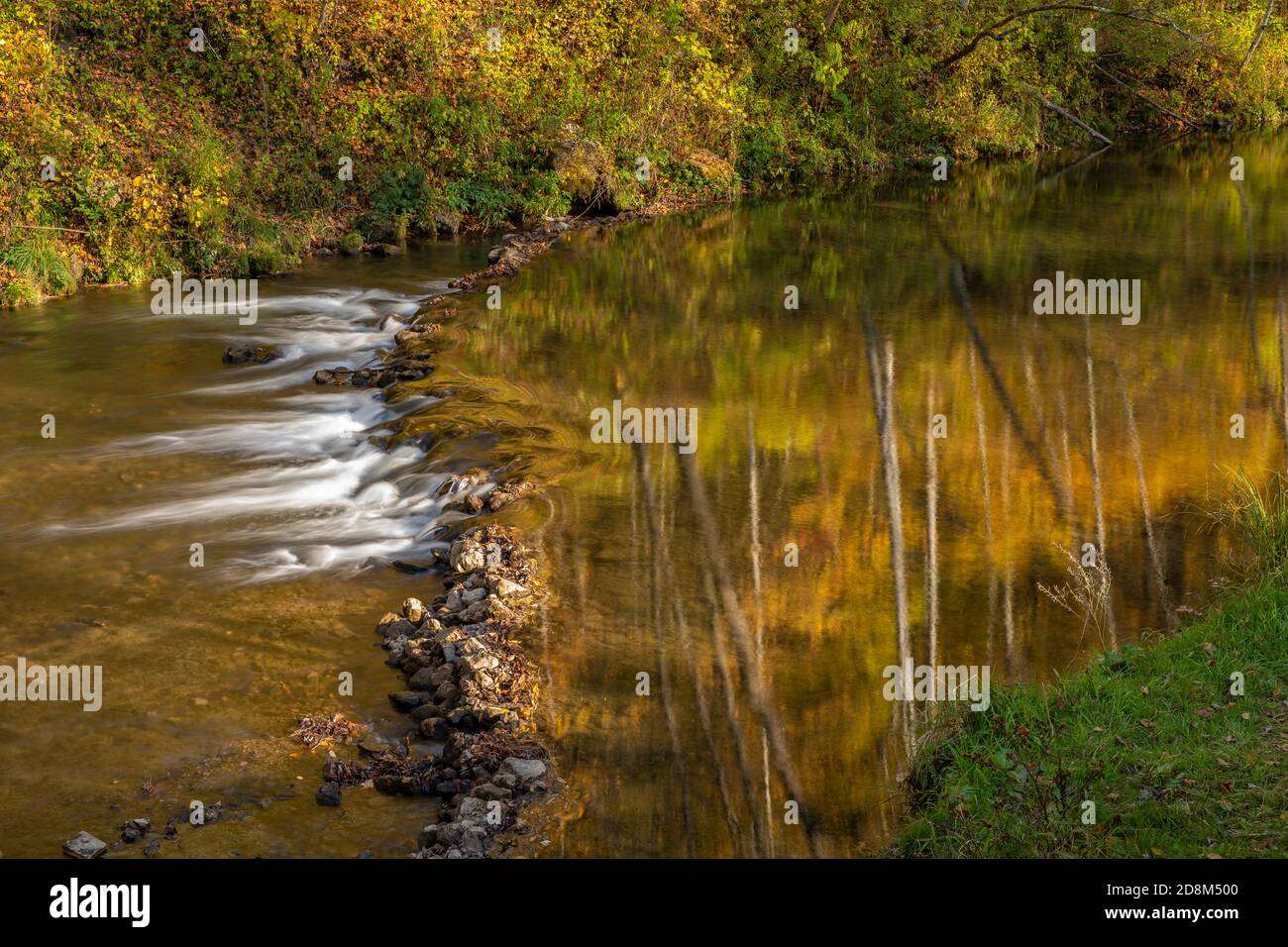 A reflective river with a rock dam in autumn Stock Photo - Alamy