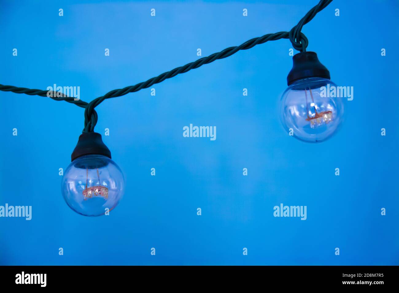 Hanging light two bulbs with glowing one different idea on light blue background. Stock Photo